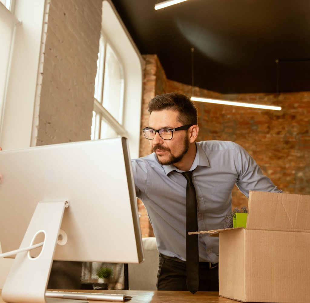 A young businessman moving in the office, getting new work place. Young caucasian male office worker equips new cabinet after promotion. Looks happy. Business, lifestyle, new life concept.